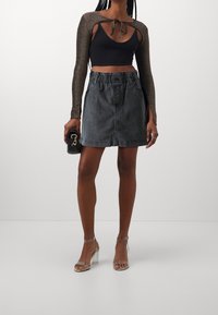 Cropped top nero con maniche lunghe metalliche, abbinato a una gonna di jeans grigia con vita elastica e tasche laterali. Sandali con tacco trasparente.