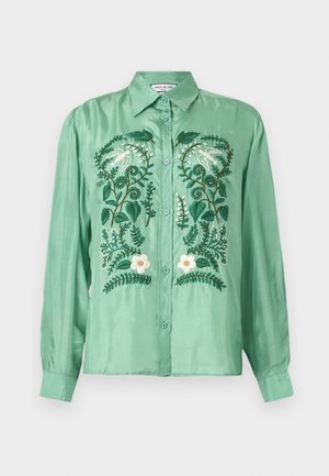 Chemise verte à manches longues avec boutons, brodée d'oiseaux blancs, de feuilles vertes et de fleurs blanches sur le devant.