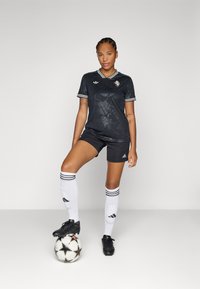Uniforme da calcio nero con design floreale, abbinato a pantaloni corti neri, calze bianche con tre righe nere e scarpette da calcio nere su una palla a fantasia.