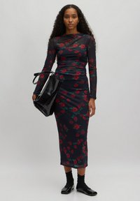 Schwarzes Blumen-Midi-Kleid mit einer taillierten Silhouette, transparenten langen Ärmeln, geschichteter Gestaltung und roten Rosenmustern. Kombiniert mit einer glänzenden schwarzen Handtasche.