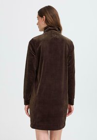 Robe en velours côtelé brun avec un col haut, des manches longues et une texture côtelée ; présente une coupe décontractée et tombe au-dessus du genou.