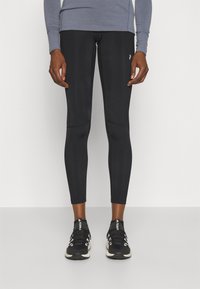 Leggings de sport noirs au design ajusté, texture lisse et accents de panneaux latéraux, associés à des chaussures de course noires.