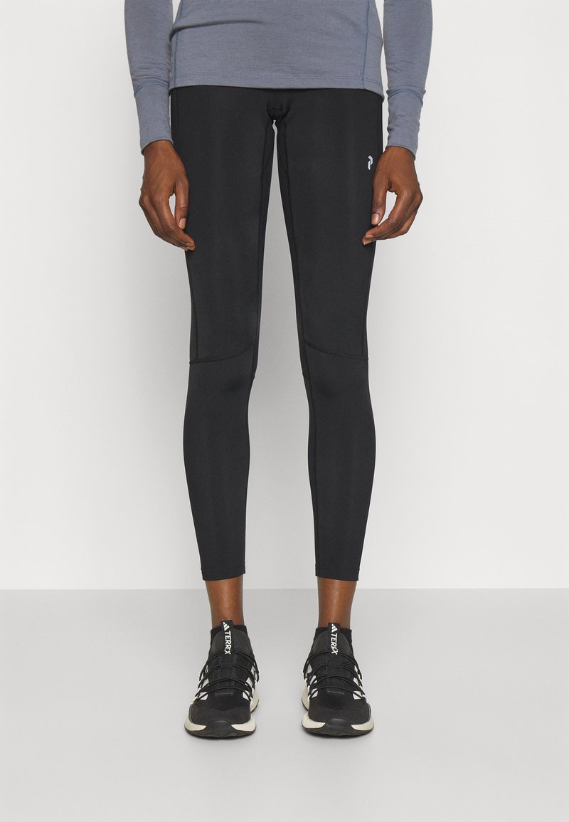 Leggings de sport noirs au design ajusté, texture lisse et accents de panneaux latéraux, associés à des chaussures de course noires.