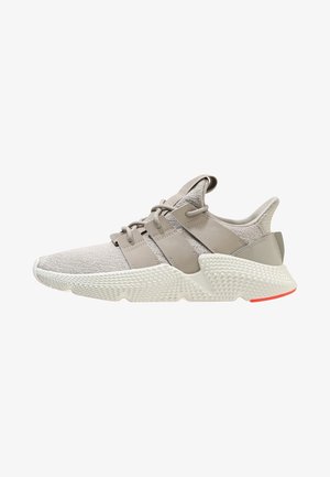 Baskets de sport gris clair avec tige en maille, semelle épaisse texturée et larges bandes de lacets, vues de profil sur fond blanc.