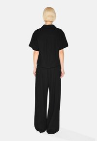 Black short-sleeve button-up shirt paired with wide-leg black trousers, featuring a relaxed fit and smooth, matte texture.