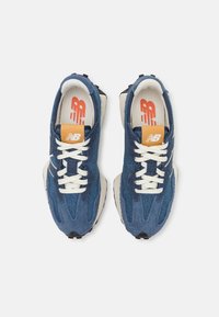 Paire de baskets New Balance en daim bleu avec lacets blancs et logo orange sur les semelles intérieures, vue de dessus sur fond blanc.