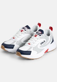Białe sportowe buty z siateczkową cholewką, granatowymi akcentami, czerwonymi detalami, gumową podeszwą i logotypem na języku. Wyróżniają się sznurowadłami i pętlą z tyłu.