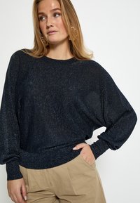 Maglione a maglia blu notte con una vestibilità ampia, maniche lunghe e orlo a coste. Una sottile trama scintillante aggiunge interesse visivo.