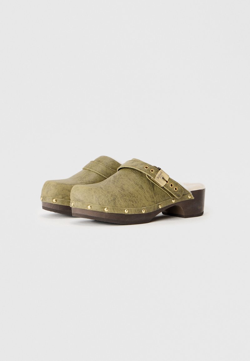 Grüne Clogs mit einer glatten Textur, Holzsohle, goldfarbene Nieten entlang der Basis und einem dekorativen Riemen mit einem Verschluss an der Seite.
