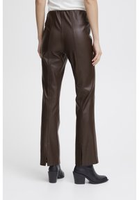 Pantalons en simili cuir marron à taille haute avec des fentes sur les côtés à l'ourlet. Le matériau a une texture lisse et une silhouette ajustée.