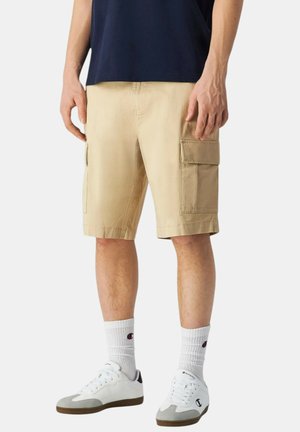 Pantaloni cargo color khaki con due tasche laterali, taglio dritto, materiale in cotone, abbinati a sneaker bianche e calzini bianchi a coste.