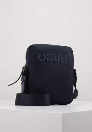 Kompaktowa czarna torebka na ramię z regulowanym paskiem, przednią kieszenią na suwak oraz wytłoczonym odwróconym napisem marki "HUGO".