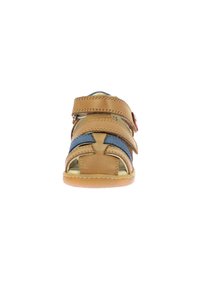 Sandale en cuir marron avec des accents bleus, deux sangles ajustables, design ouvert à l'avant et semelle en caoutchouc. Elle présente un contour cousu et un détail en bouton.