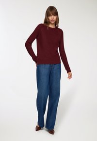 Burgundowa dzianinowa sweter o prążkowanej fakturze, okrągłym dekolcie i długich rękawach, zestawiony z niebieskimi dżinsami o wysokim stanie w szerokim kroju.