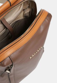 Bruine leren tas met een tan leren accent, bovenrits en een binnenzak. Heeft een gladde textuur en gouden hardware details.
