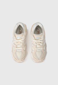 Par de ténis de corrida New Balance em bege e branco com detalhes em malha e camurça, vistos de cima sobre um fundo branco.