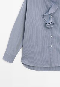 Chemise bleu clair à manches longues avec fines rayures verticales, boutons blancs, manches avec poignets et un détail volanté près du col.
