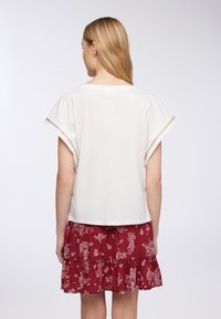 Top bianco in cotone con maniche a dolman corte e scollatura rotonda, abbinato a una gonna a strati con stampa floreale rossa.