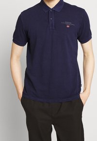 Marineblå bomulds polo-shirt med korte ærmer, to-knaps lukning og broderet logo på brystet. Glat tekstur og afslappet pasform.