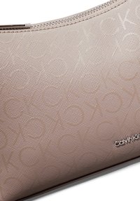 Kosmetyczka Calvin Klein w jasnoróżowym, teksturowanym materiale z wytłaczanym wzorem logo, wyposażona w srebrny zamek błyskawiczny i eleganckie akcenty metalowe.