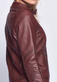 Mujer vistiendo una chaqueta de cuero burdeos ajustada con costuras detalladas y un bolsillo con cremallera en el lateral.