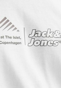 Balta medvilninė marškinėlė su pilka užrašu "Jack & Jones" ir papildomu tekstu viršuje, kairėje pusėje esant geometriškai grafikai.