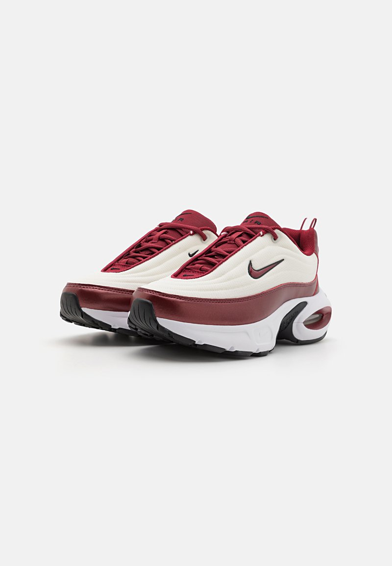 Sneakers Nike rossi e crema con una parte superiore testurizzata, design con lacci e una suola con un'ammortizzazione prominente. Dettagli neri e logo.