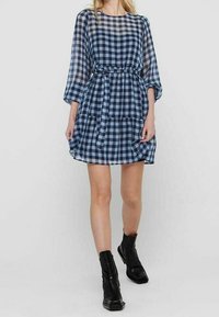 Blau-weißer karierter Kleid mit Dreiviertelärmeln, gerafftem Bund, fließendem Rock und einem Bindegürtel, kombiniert mit schwarzen Stiefeletten.
