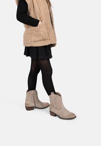 Botas de tobillo de ante beige con punta ligeramente afilada, costuras decorativas y un bajo tacón de madera. Acabado texturizado con cremallera lateral.
