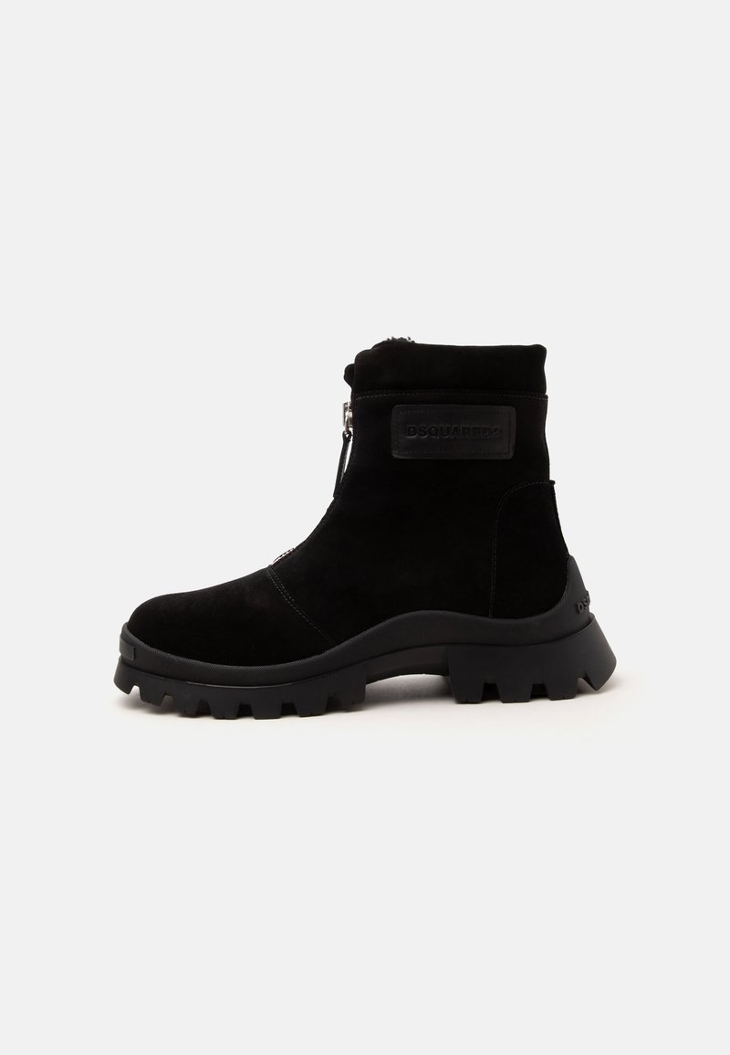 Bottine noire avec semelle épaisse à crampons, fermeture éclair latérale et patch de marque sur la cheville extérieure, en matériau semblable au daim.