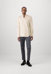 Svetlo béžová košeľa na gombíky, slim fit, z bavlnenej látky; v kombinácii s tmavošedými nohavicami a lesklými čiernymi topánkami. Minimalistické logo na košeli.