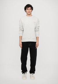 Light gray sweatshirt with ribbed cuffs and hem, featuring embossed "CLOSED" logo. Black pants and light-colored sneakers complete the outfit.