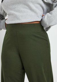 Olivgrön, högmidjade byxor i ett slätt, stretchigt material. Har en ren, minimalistisk design utan synlig hårdvara eller mönster.