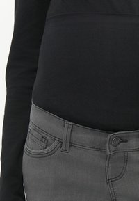 Maglia nera a maniche lunghe abbinata a jeans grigi caratterizzati da una trama liscia, un design a cinque tasche e una chiusura con bottone in vita.