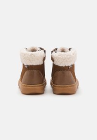 Stivaletti alla caviglia in suede marrone con un collare bianco soffice, cerniera laterale e suola in gomma texture. Il design presenta dettagli cuciti.