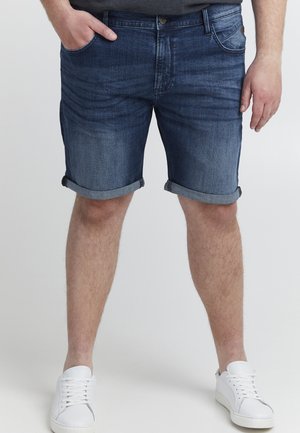 Mörkblå denimshorts med en urtvättad finish, uppvikta nederkant, fem fickors design och metallknapp, i kombination med vita sneakers.