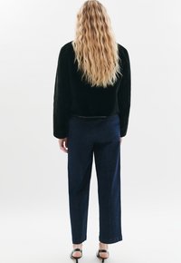 Zwarte faux fur kortjasje met lange mouwen, gecombineerd met donkerblauwe wijde spijkerbroek en zwarte hoge hakken.
