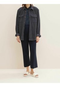 Dark gray corduroy overshirt with two chest pockets, paired with navy slim-fit trousers and white slide sandals.