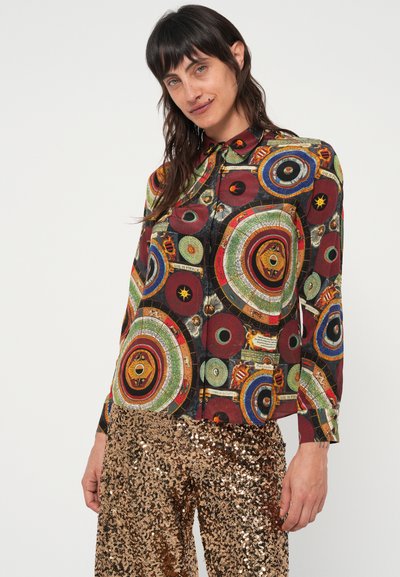Button-up shirt met een meerkleurig cirkelpatroon op een zwarte achtergrond; aangevuld met glanzende gouden paillettenbroek.