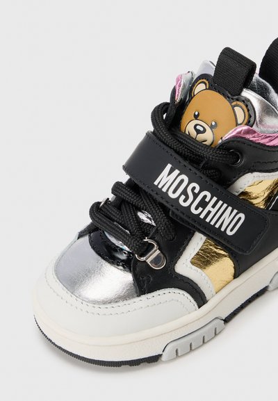 Basket en cuir noir avec des accents argent et or, présentant un ours en cartoon sur la languette, un bout rond et une sangle Velcro avec le logo "MOSCHINO".