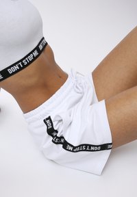 Pantaloni corti sportivi bianchi con vita elastica, caratterizzati da una fascia di testo nera con la scritta "NON FERMARE ME." Texture liscia con vestibilità comoda.