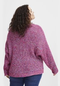 Överdimensionerad tröja i rosa heathered stickad tyg. Har neddragna axlar, ribbad struktur och en något rundad nederkant. Stylad med mörka jeans.