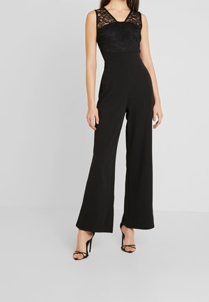 Black jumpsuit with a lace bodice, wide-leg trousers, and a fitted waist. Features a v-neckline and is paired with strappy high heels.