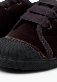 Scarpe con suola in gomma nera e tomaia in velluto viola scuro, con occhielli rotondi e lacci in tessuto. Parte anteriore strutturata e protezione per le punte.