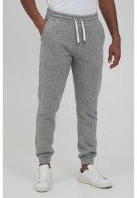 Gray jogger pants made of soft fabric, featuring an elastic waistband with drawstrings and ribbed ankle cuffs. Worn with white sneakers.