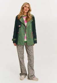 Zelená a námořnická bunda s růžovými akcenty, nad svrchním pruhovaným svetrem. Béžové kalhoty s leopardím vzorem, doplněné světlou obuví.