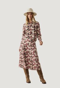 Conjunto con estampado floral que incluye una blusa de cuello y mangas largas y una falda larga a juego en rosa, acompañados de botas marrón tierra hasta la rodilla.