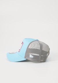 Gorra de color azul claro con una parte posterior de malla gris, visera curvada y un parche de logo prominente en el frente. Cuenta con un cierre tipo snapback para ajustabilidad.