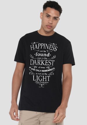 Young man wearing a black t-shirt with white text quoting Albus Dumbledore about finding happiness in darkest times by turning on the light.