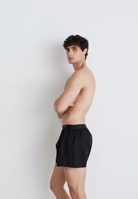 Schwarze Shorts mit einem elastischen Bund, aus leichtem Material gefertigt. Das Design verfügt über seitliche Taschen und eine lockere Passform.